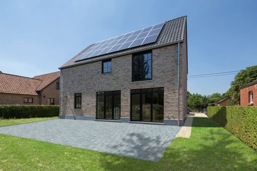 Freistehendes Backsteinhaus mit Solarmodulen auf dem Dach und Rasenfläche